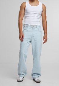 Ljusblå denimjeans med avslappnad passform, fem fickor och dragkedja. Kombineras med en vit linne och svart/vita sneakers.