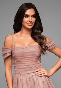 Robe rose blush avec un corsage froncé, des manches épaules dénudées et une jupe fluide avec une texture légèrement brillante.