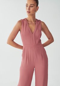 Roze jumpsuit met een V-halslijn, mouwloos ontwerp en een aansluitende taille. Gemaakt van soepele stof, met een casual silhouet.