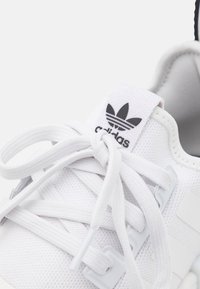 Närbild av vit Adidas-sneaker med knutna snören och svart trefoil-logga på tungan.