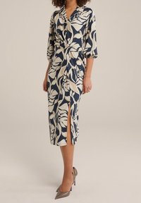 Kleid mit navyblauem und cremefarbenem Blättermuster, Wickeldesign, Dreiviertelärmel und seitlichem Schlitz; aus strukturiertem Stoff.