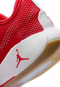 Talons de chaussure de basketball rouge et blanc avec logo Jumpman rouge sur une semelle intermédiaire blanche et semelle extérieure en caoutchouc orange texturée visible.