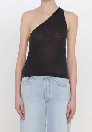 Persoon die een mouwloze zwarte top met één schouder en lichtblauwe, hoog getailleerde jeans draagt, staat met ontspannen armen langs het lichaam.