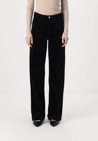 Pantalon en velours côtelé noir à coupe droite, avec une taille classique, des poches latérales et une texture douce. Assorti à un haut beige à côtes.
