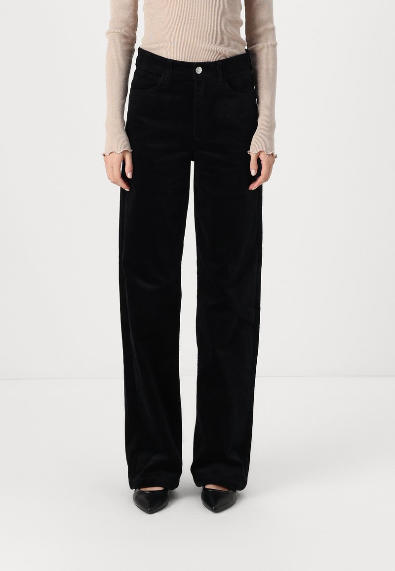Pantalon en velours côtelé noir à coupe droite, avec une taille classique, des poches latérales et une texture douce. Assorti à un haut beige à côtes.