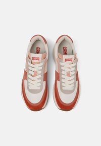 Sneakers z białą tkaniną na wierzchu, z akcentami z brzoskwiniowego i różowego zamszu, okrągłym noskiem i białymi sznurowadłami. Zawierają branding "CAMPER" na języku.