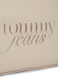 Εμπριμέ λογότυπο "tommy jeans" σε μπεζ δερμάτινη επιφάνεια με λεία υφή και διακριτική σκιά στο κάτω άκρο.
