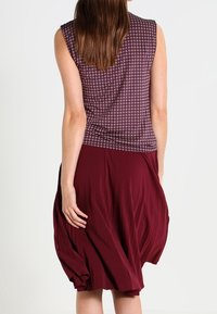 Top senza maniche in tessuto bordeaux a fantasia abbinato a una gonna fluida bordeaux, con morbide plissettature e un design drappeggiato.