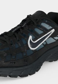 Μαύρο και μπλε αθλητικό παπούτσι Nike για τρέξιμο με επενδύσεις από δίχτυ, μαύρα κορδόνια και λευκό κεντημένο λογότυπο Nike στην πλευρά.
