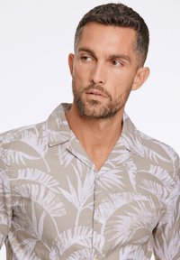 Korte mouwen overhemd in beige met witte palmbladenprint, voorzien van een camp collar en subtiele knoopdetails. Lichtgewicht stof met een ontspannen pasvorm.