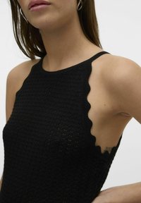 Top senza maniche nera lavorata a maglia con bordi scallop, caratterizzato da un motivo testurizzato e un design aderente.