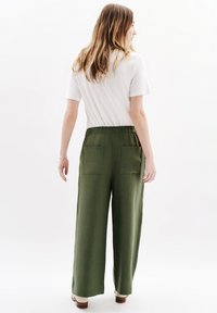 Pantalones de pierna ancha verdes con una cintura alta y dos bolsillos traseros, exhibidos en un modelo que lleva una camiseta blanca sencilla. Textura suave.