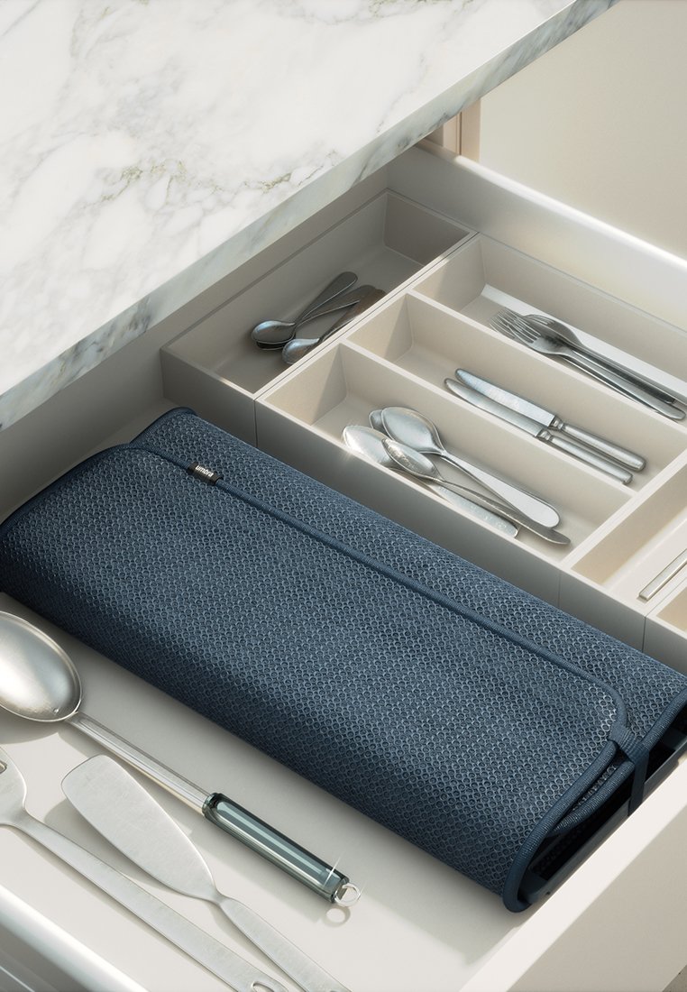 Dunkelblauer texturierter Besteckorganizer, der in einer Schublade platziert ist, mit silbernem Besteck, das ordentlich neben ihm auf einer hellbeigen Unterlage angeordnet ist.
