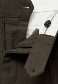 Tissu vert olive foncé avec une texture douce, comportant une poche zippée, un bouton noir et des accents de col blancs contrastants.