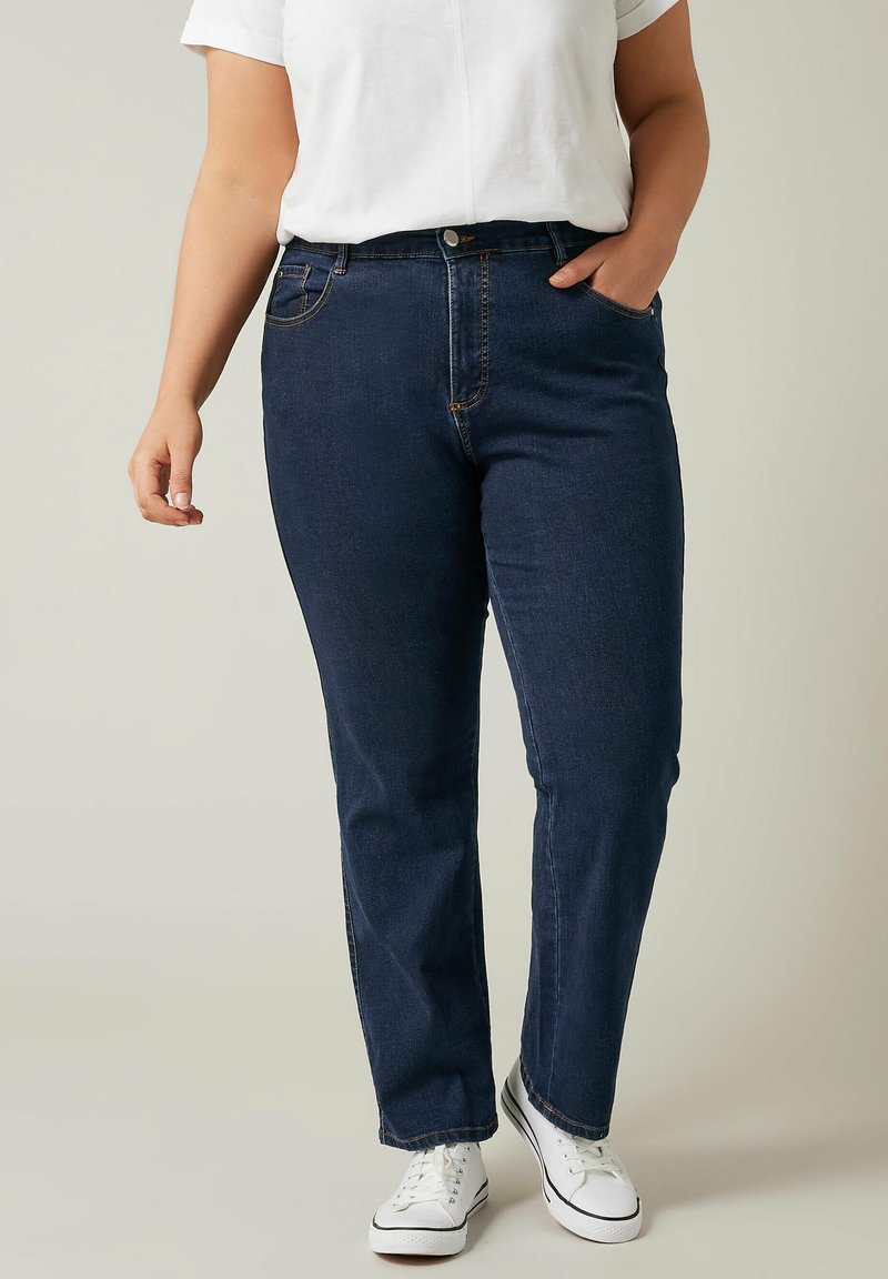 Jeans in denim blu scuro, con un classico design a gamba dritta, tasche frontali e chiusura con bottone. Indossati con una t-shirt bianca e sneakers.
