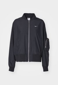 Zwarte nylon bomberjack met een opstaande kraag, elastische manchetten, een rits aan de voorkant en een ritszak op de arm. Bevat een Nike-logo op de borst.