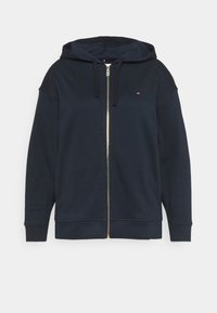 Sweat à capuche bleu marine avec fermeture éclair, fabriqué en tissu doux, doté d'une capuche, de manches longues et d'un petit logo sur la poitrine. Détail de la fermeture éclair dorée.