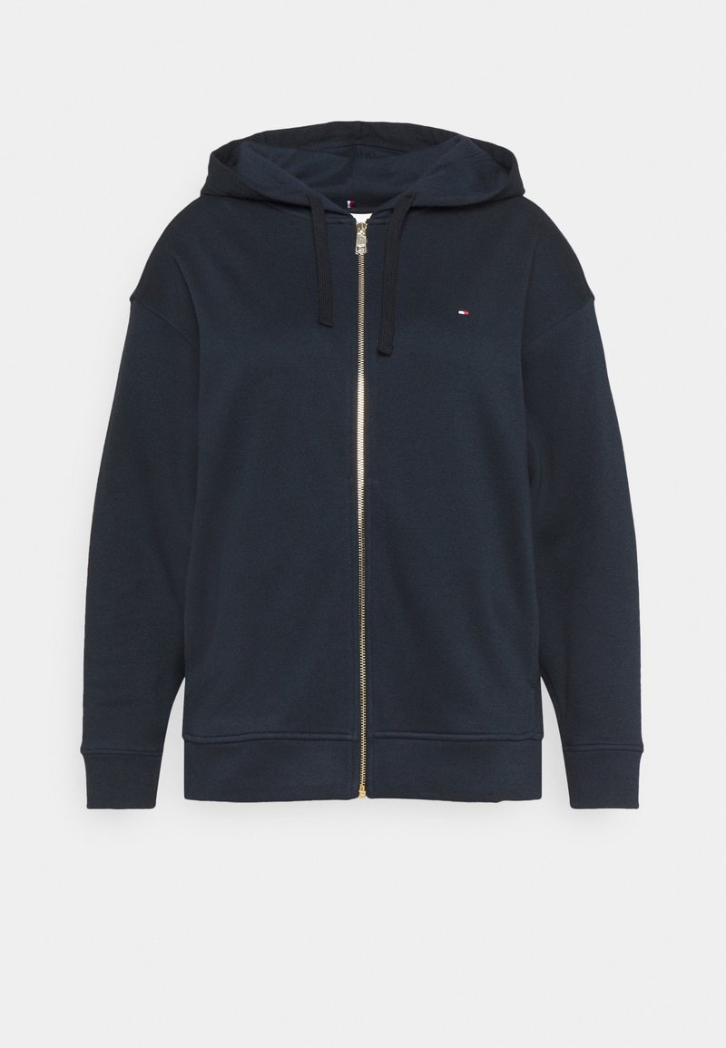 Sweat à capuche bleu marine avec fermeture éclair, fabriqué en tissu doux, doté d'une capuche, de manches longues et d'un petit logo sur la poitrine. Détail de la fermeture éclair dorée.