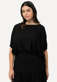 Robe noire fluide avec un décolleté large et des manches courtes. Dotée d'une taille élastique et d'un bas à volants pour plus de texture.