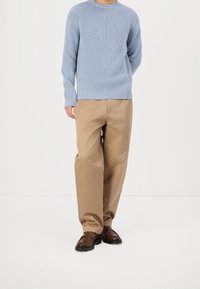 Light blue ribbed sweater with a round neckline, paired with loose beige trousers and brown loafers, standing on a neutral background.