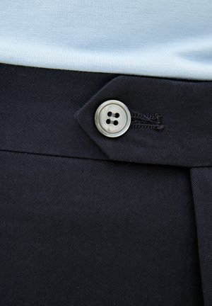 Zwarte broek met een gladde textuur heeft een zilveren knoop met vier gaten. De taille heeft een schuin flap en subtiele stikdetails.