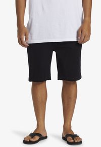 Black cotton shorts with a relaxed fit, hemmed edges, and a smooth texture, worn above the knee, paired with black flip-flops.