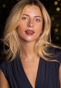 Stříbrný náhrdelník s řetízkem, který obsahuje čtvercové a hvězdicové akcenty. Model má vlnité blond vlasy a nosí tmavě modrý top.