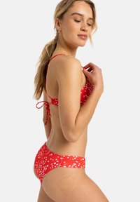 Red bikini with white floral pattern. Ties at the back, adjustable straps, and a fitted style. Smooth fabric with a slight sheen.