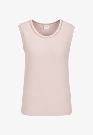 Frau steht vor einer beigen Wand und trägt ein ärmelloses, hellrosa Oberteil, weiße, verkürzte Hose mit geknöpften Manschetten, silberne High-Heel-Sandalen und auffällige Ohrringe.