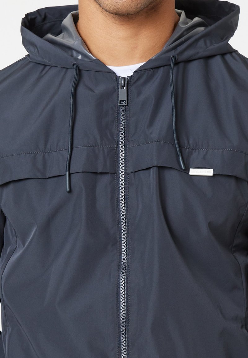 Maritime windbreakerjas gemaakt van lichtgewicht, waterafstotende stof. Voorzien van een ritssluiting aan de voorkant, een capuchon en een logo-opname op de borst.