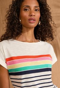 T-shirt rayé avec une base blanche, ornée de bandes horizontales colorées en rouge, rose, jaune, vert et bleu marine. Manches courtes et col rond.