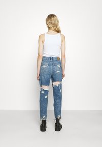 Ljusblå, slitna jeans med rips vid knäna och fransade fållar, i kombination med en vit linne och svarta ankelskor.