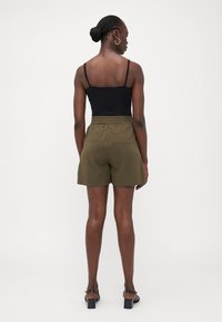 Black camisole top, olive green shorts with elastic waistband, smooth texture, above-knee length, paired with black heeled sandals.