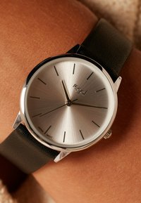 Silberne Analog-Uhr mit gebürstetem Metallzifferblatt, minimalen Stundenmarkierungen und schwarzem, strukturiertem Lederarmband, ausgestattet mit einem Gehäuse aus Edelstahl.