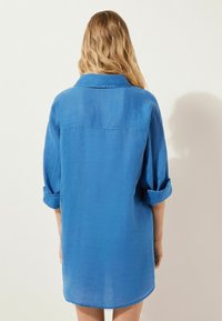 Blå linneskjorta med uppvikt ärmdesign, har en bakstycke och en lätt rundad nederkant. Mjuk textur och lätt utseende.