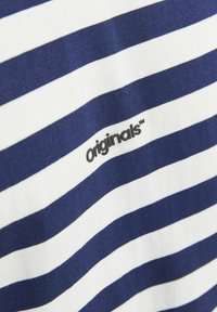Jūras spēku un baltu svītrainu krekls, kas izgatavots no mīkstas auduma; ir neliels melns "originals" logo kreisajā apakšējā stūrī.