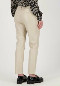 Broek in zacht beige fauxleer, smal gesneden, met achterzakken. Gecombineerd met zwarte loafers met een gouden accent.