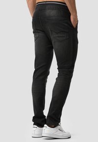 Jean en denim noir avec une coupe slim, une ceinture élastique et deux poches arrière. Assortie avec des baskets blanches avec des accents noirs.