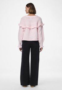 Pull en moelleux rose pâle, orné d'un accent volant au niveau du col et des poignets, associé à un pantalon noir à jambes larges. Texture douce et coupe ample.