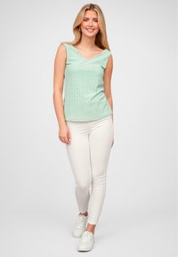 Top mint vernil fără mâneci, cu decolteu în V, cu detalii din dantelă. Asortat cu pantaloni albaștri slim-fit și adidași albi.
