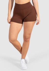 Bruine hooggetailleerde shorts van rekbaar materiaal, met een gladde textuur en een aansluitend ontwerp, gecombineerd met witte sportschoenen.