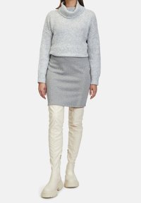 Szary sweter z golfem w splot kabelkowy, dopasowana szara spódnica w kratkę houndstooth oraz kremowe kozaki do kolan z gumową podeszwą i zamkami błyskawicznymi.