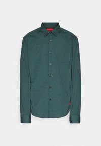 Chemise vert foncé à manches longues avec col, boutons noirs et une petite étiquette rouge sur la couture latérale inférieure.