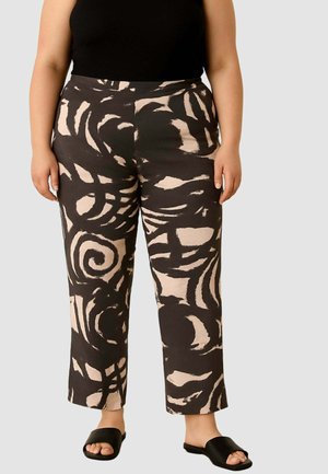 Pantaloni neri e beige a motivi con un design a spirale, taglio dritto e texture liscia, abbinati a sandali neri senza tacco e una maglia aderente.