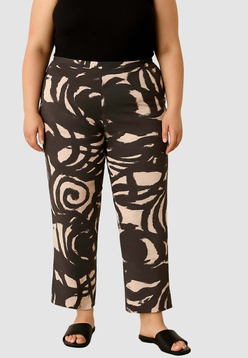 Pantaloni neri e beige a motivi con un design a spirale, taglio dritto e texture liscia, abbinati a sandali neri senza tacco e una maglia aderente.