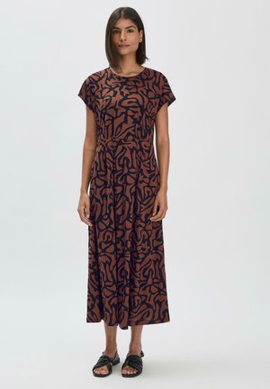 Kleid in mittellanger Form mit dunklem Marineblau als Grundfarbe und wirbelndem braunem abstraktem Muster. Kurze Ärmel, lockere Passform, weicher Stoff, kombiniert mit schwarzen Sandalen.