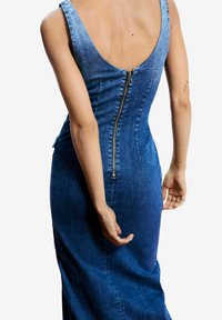 Rochie din denim cu croială mulată, spate adânc decupat în formă de scobitură și închidere cu fermoar pe spate. Materialul are o nuanță albastră în gradient și o textură netedă.