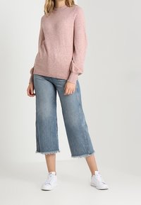 Světle růžový pletený svetr s dlouhými rukávy, kombinovaný se světle modrými zkrácenými džíny s třepenými okraji. Bílá teniska dotváří celkový look.
