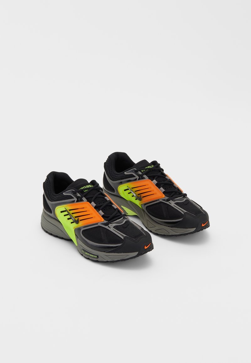 Paire de chaussures de sport noires avec des superpositions vert fluo et orange, semelles grises et petits logos Nike orange sur les orteils.