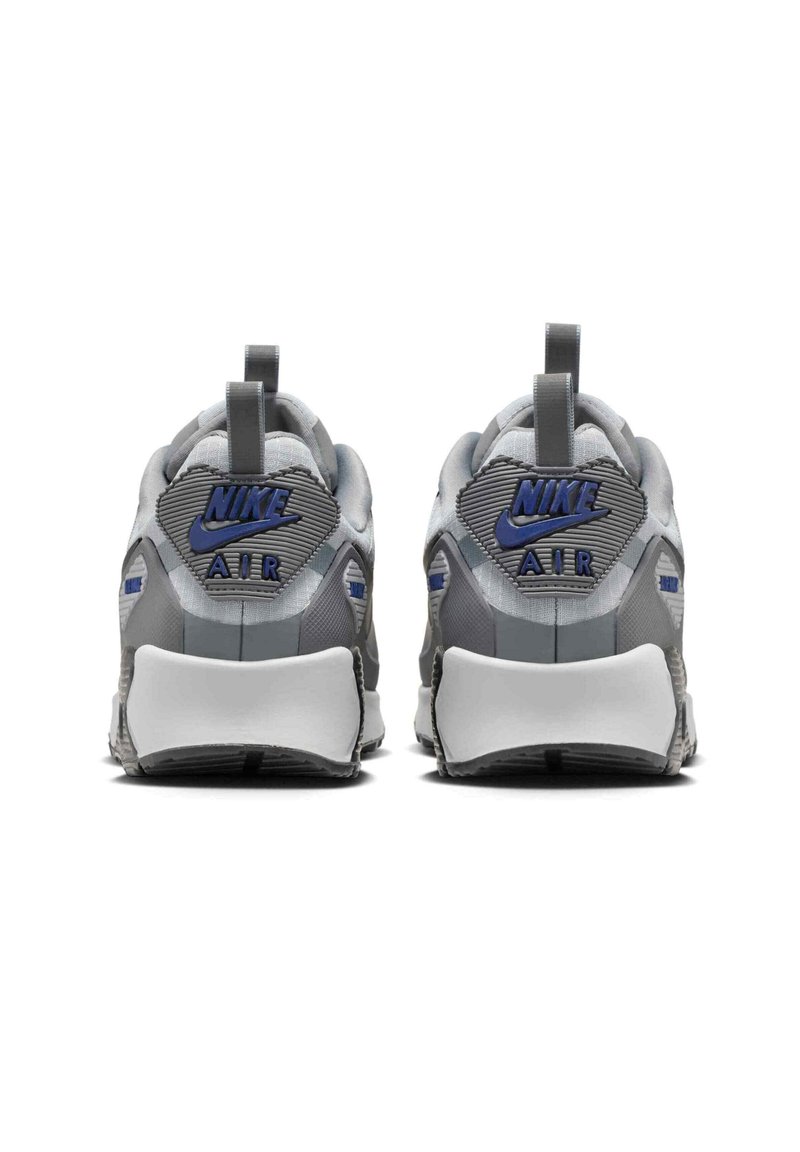 Paire de baskets Nike Air grises vues de dos avec des logos Nike bleus et des languettes d'extraction sur un fond blanc.